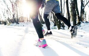 three runs dressed in full winter clothing, running along a snowy trail